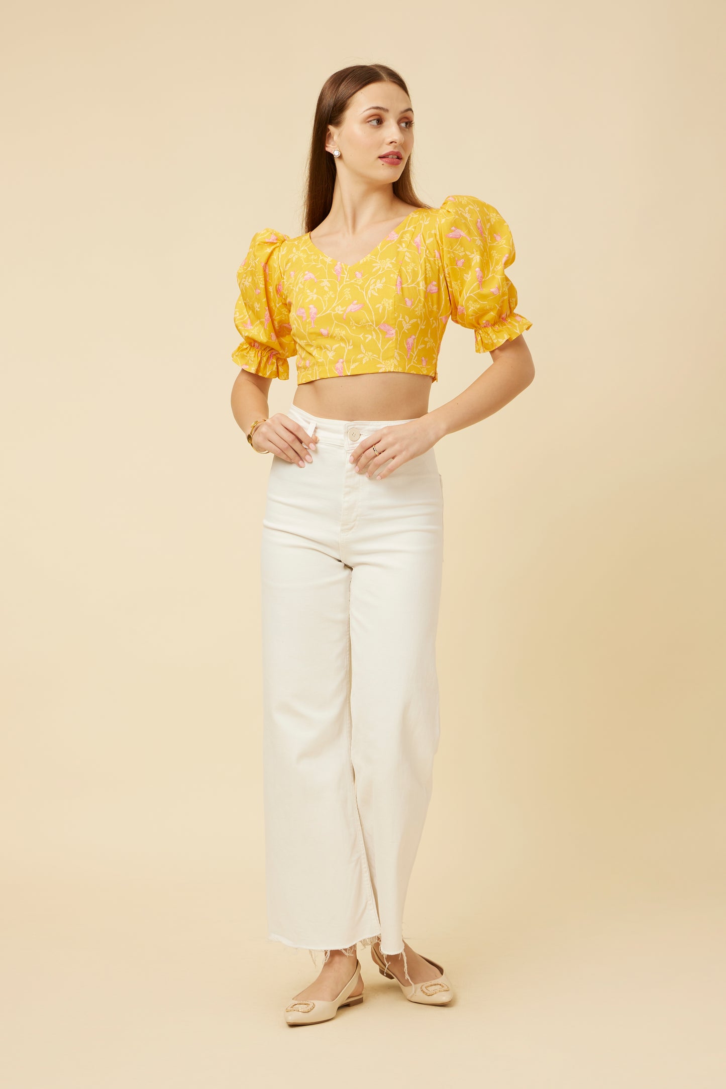 Straight-standing model showcasing the Peela Sunshine Crop Top's V-neck front and criss-cross tie-back design, paired with white pants