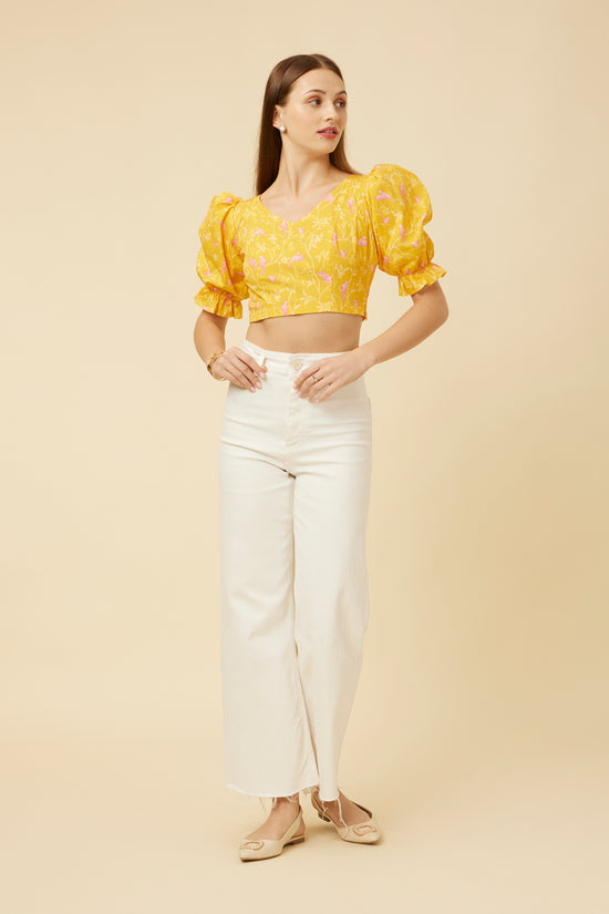 Straight-standing model showcasing the Peela Sunshine Crop Top's V-neck front and criss-cross tie-back design, paired with white pants