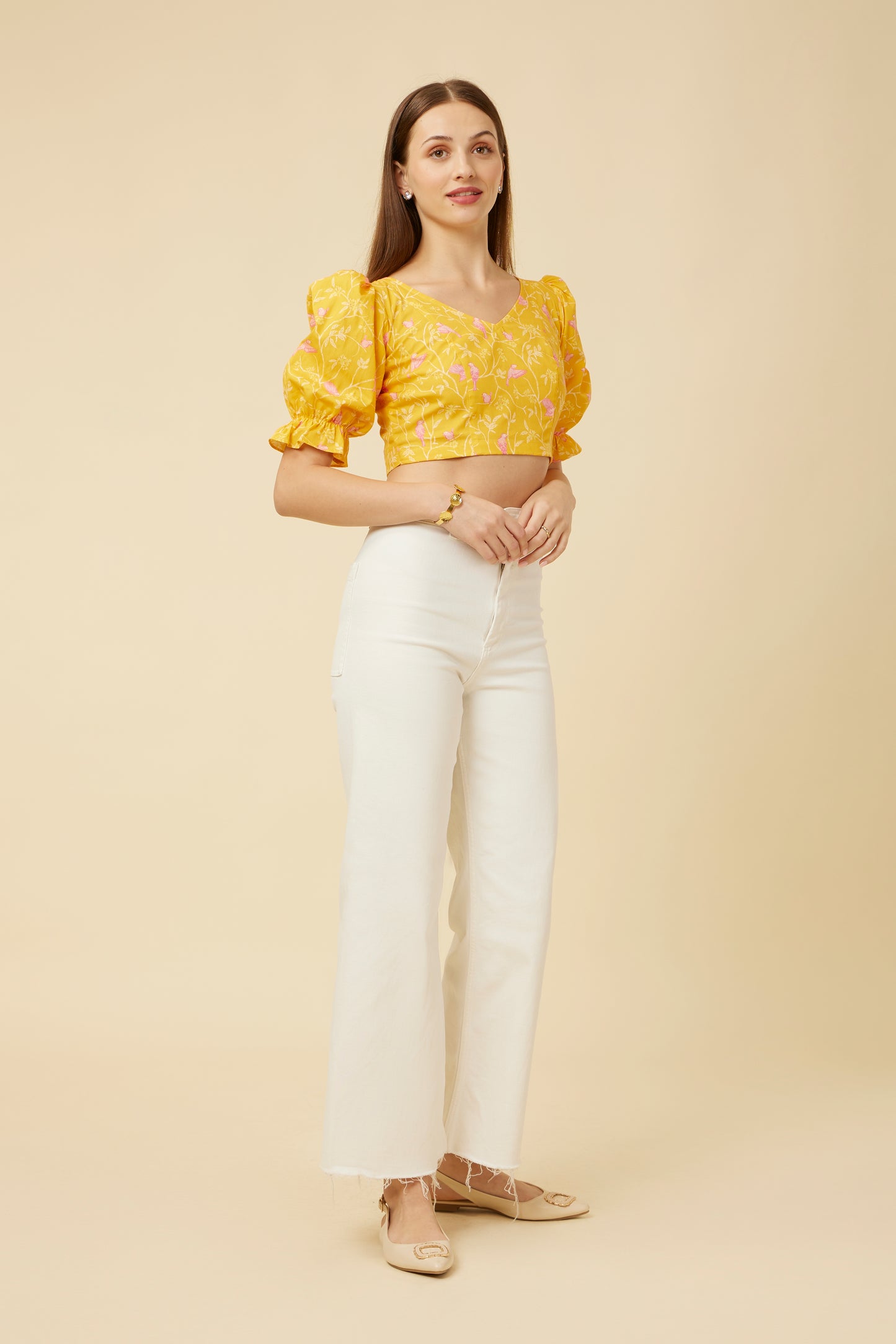 Three-quarter view of a model in the Peela Sunshine Crop Top, featuring a unique back design and paired with elegant white pants for a bright outfit