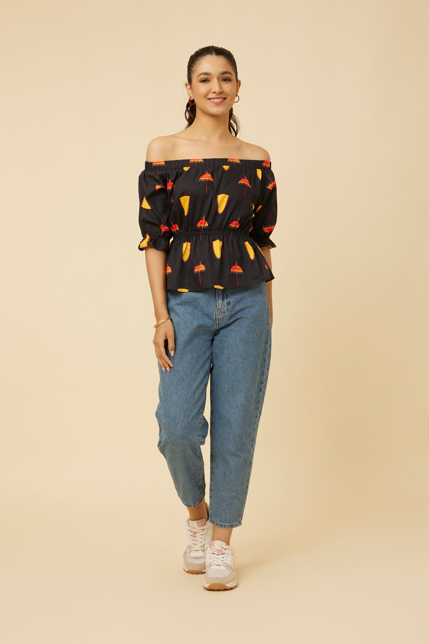 Full-length image of a model in a Spree in Black Off-Shoulder Top paired with blue jeans, showcasing the extended length and snug elastic off-shoulder design