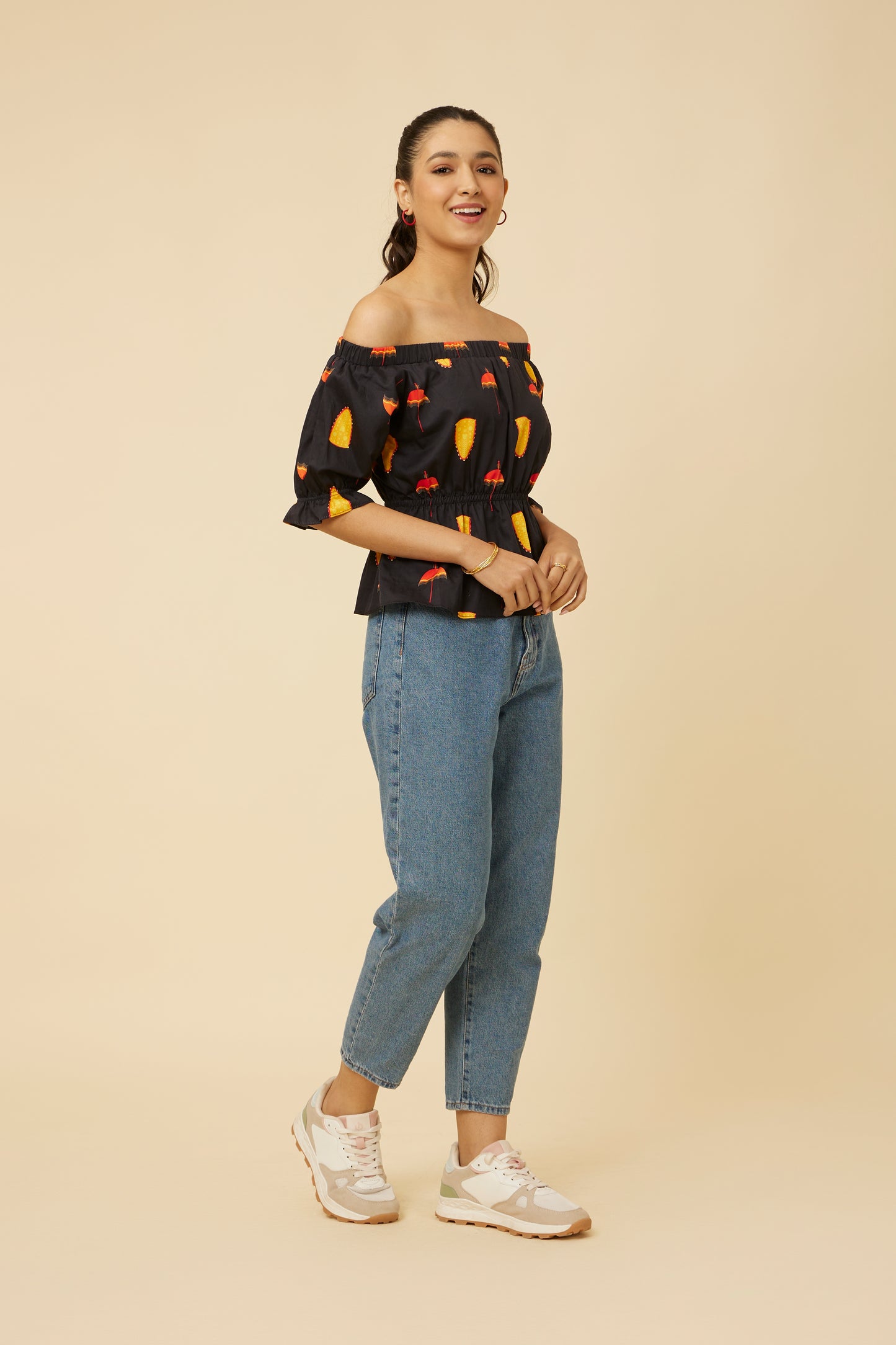 Side view of the Spree in Black Off-Shoulder Top, highlighting the cinched waist and 3/4 balloon sleeves, adorned with vibrant cultural motifs