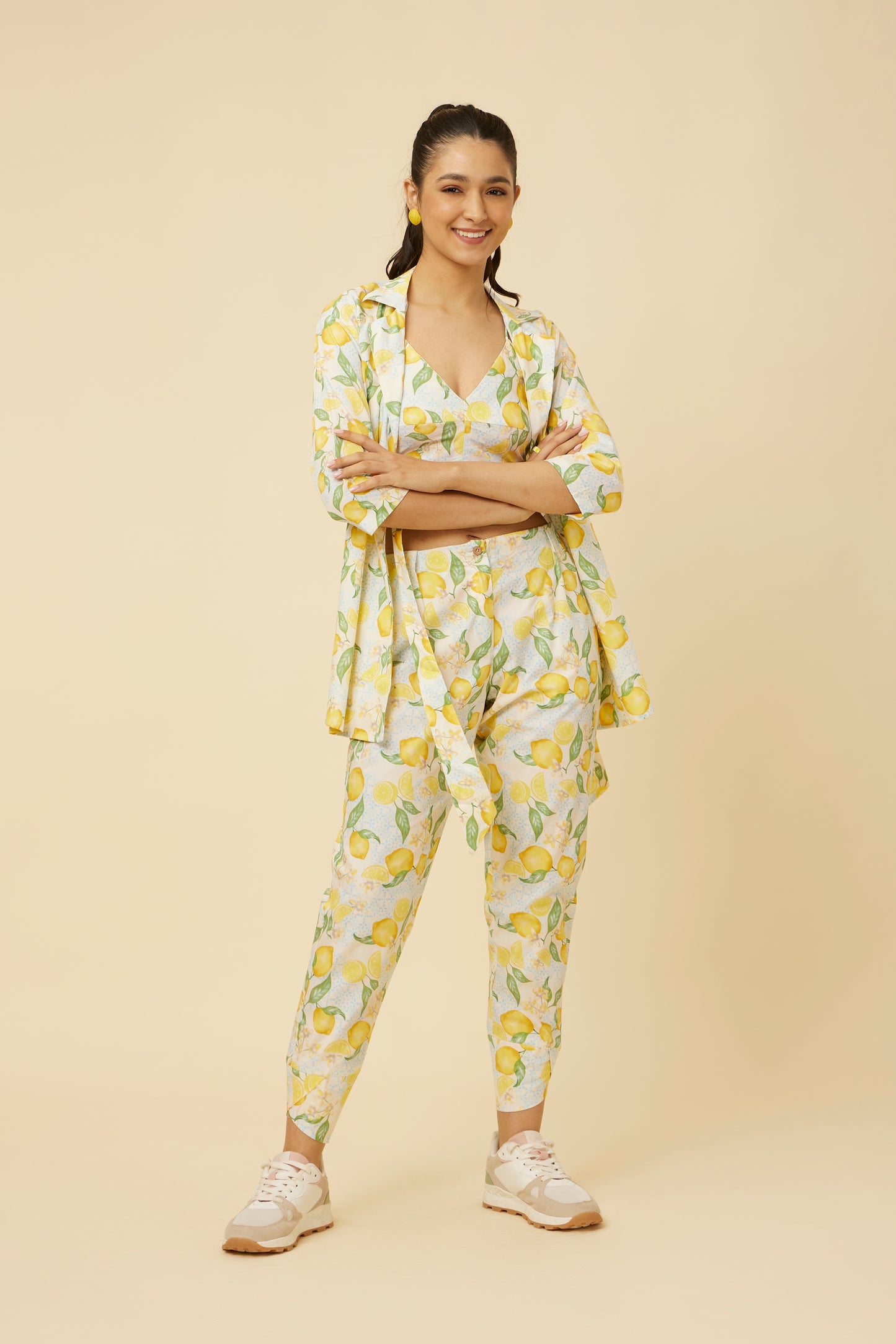 Model radiates in the Citrus Dream Co-Ord Set featuring a shirt-jacket hybrid top with side-tie design, paired with fitted pants showcasing a stylish tulip hem, all in a lively lemon tile print against a white backdrop.