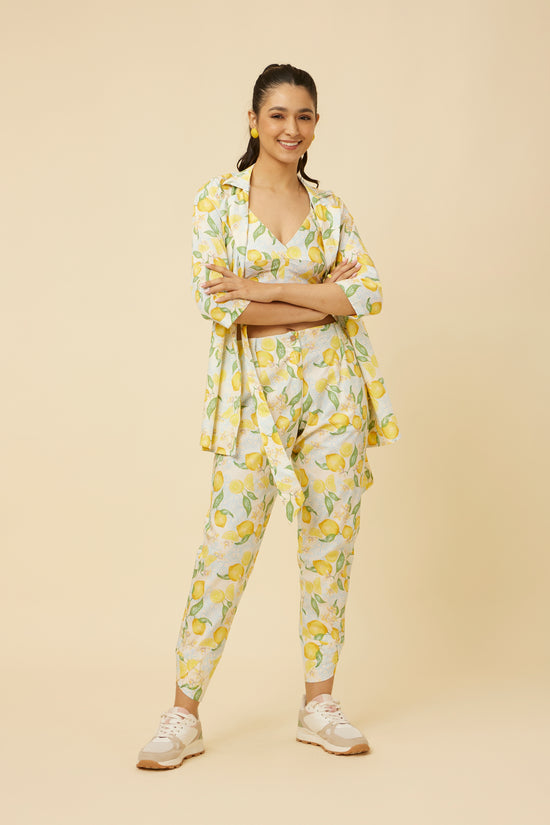 Model radiates in the Citrus Dream Co-Ord Set featuring a shirt-jacket hybrid top with side-tie design, paired with fitted pants showcasing a stylish tulip hem, all in a lively lemon tile print against a white backdrop.