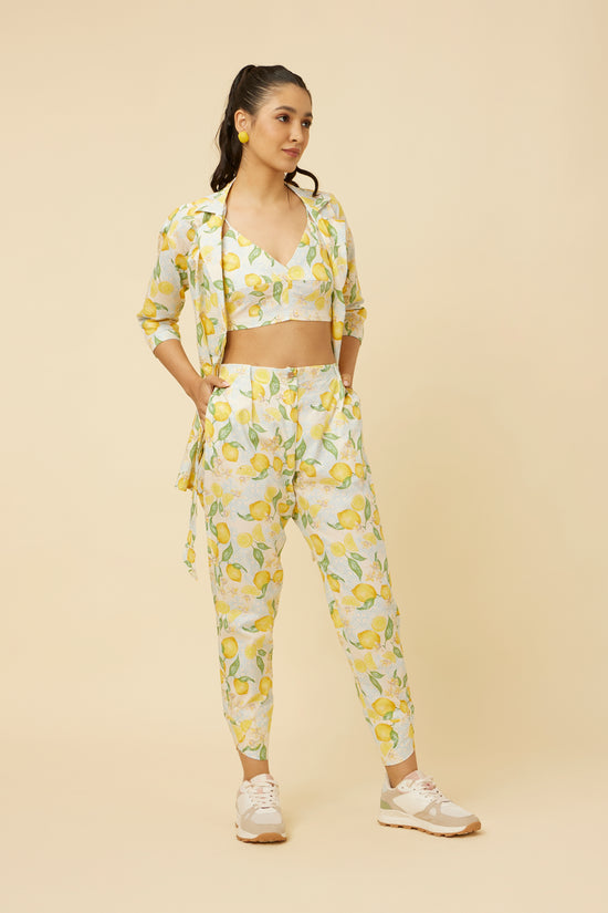 Confident stance in the Citrus Dream Co-Ord Set, detailing the vibrant lemon print top with an innovative side-tie and fitted pants with tulip hem, accented by practical side pockets, embodying a blend of style and functionality.