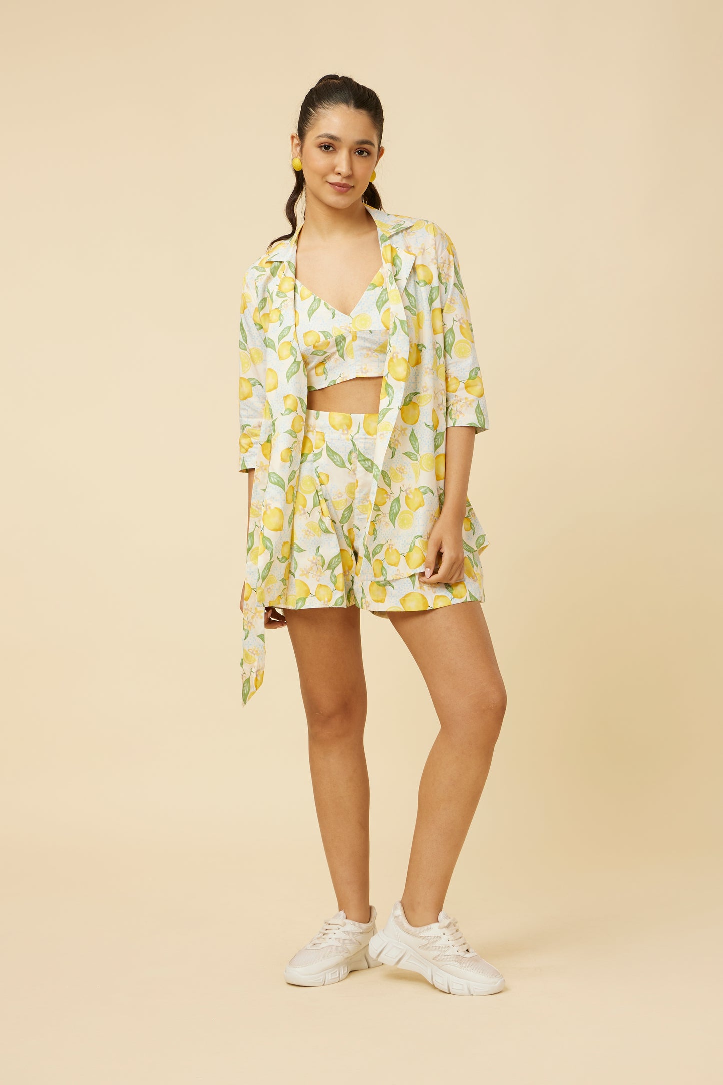 Model displays the Citrus Dream Shirt & Shorts Co-Ord Set, featuring a lively lemon tile print. The shirt’s side-tie design adds a unique twist to the shirt-jacket hybrid style, while the shorts ensure comfort with side pockets and back elastic.