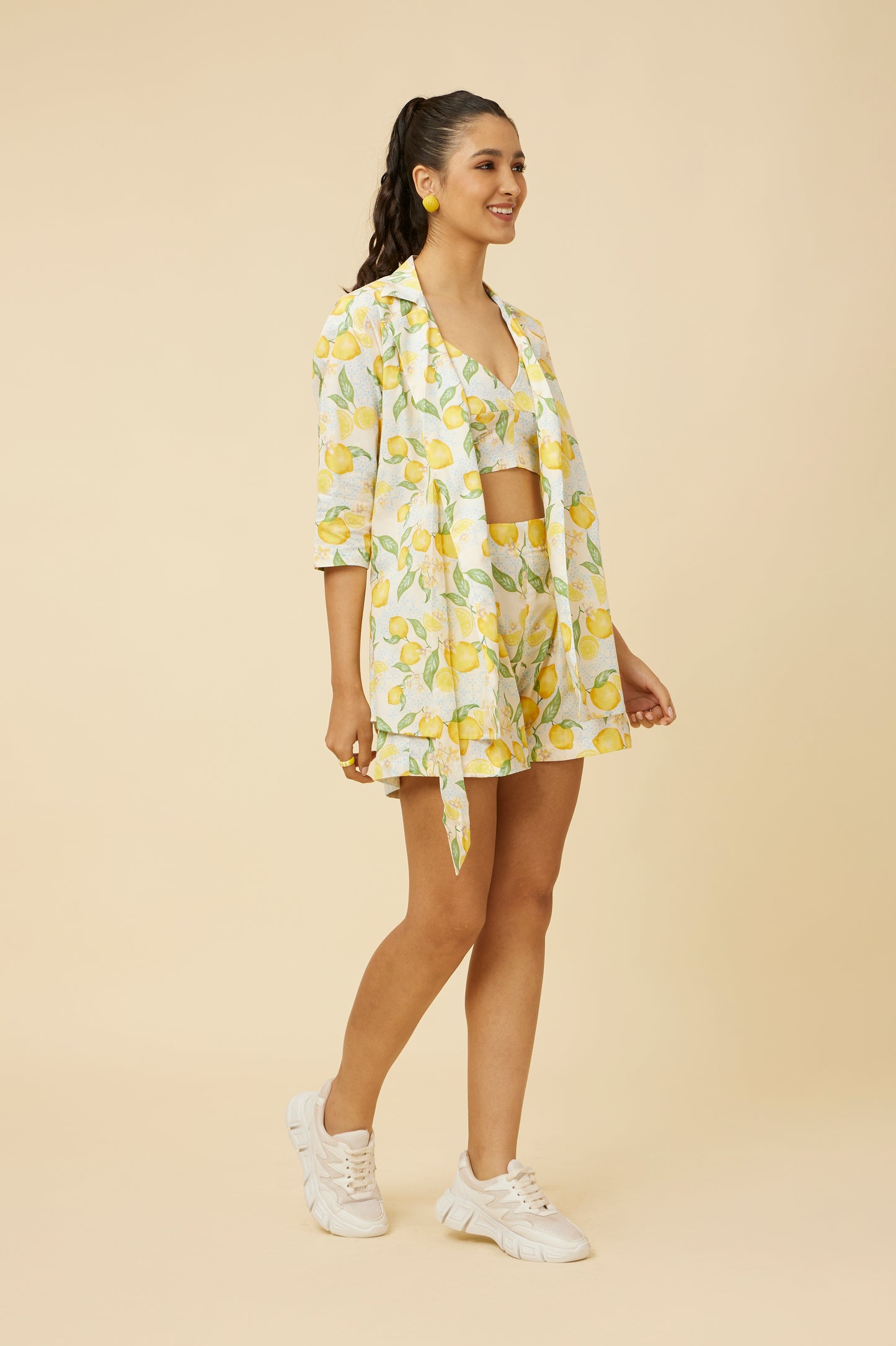 Chic model in the Citrus Dream Co-Ord Set exudes summer vibes with the shirt's versatile side-tie design and the matching shorts, both adorned with a zesty lemon print, perfect for a fresh seasonal update to any wardrobe.