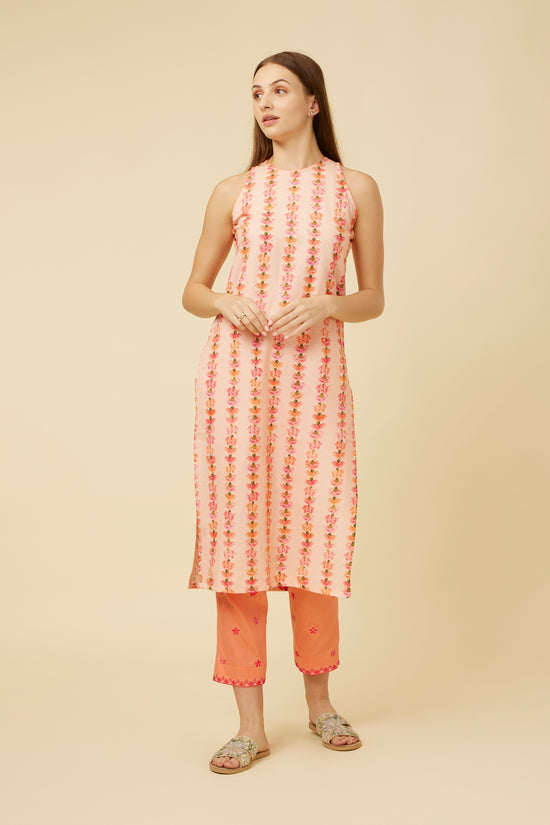 The model stands facing forward, showcasing the front of the 'Gulabi Garden Kurta,' with its fitted bodice and gentle flare towards the hem, accentuating the vertical carnation pattern against the pink backdrop