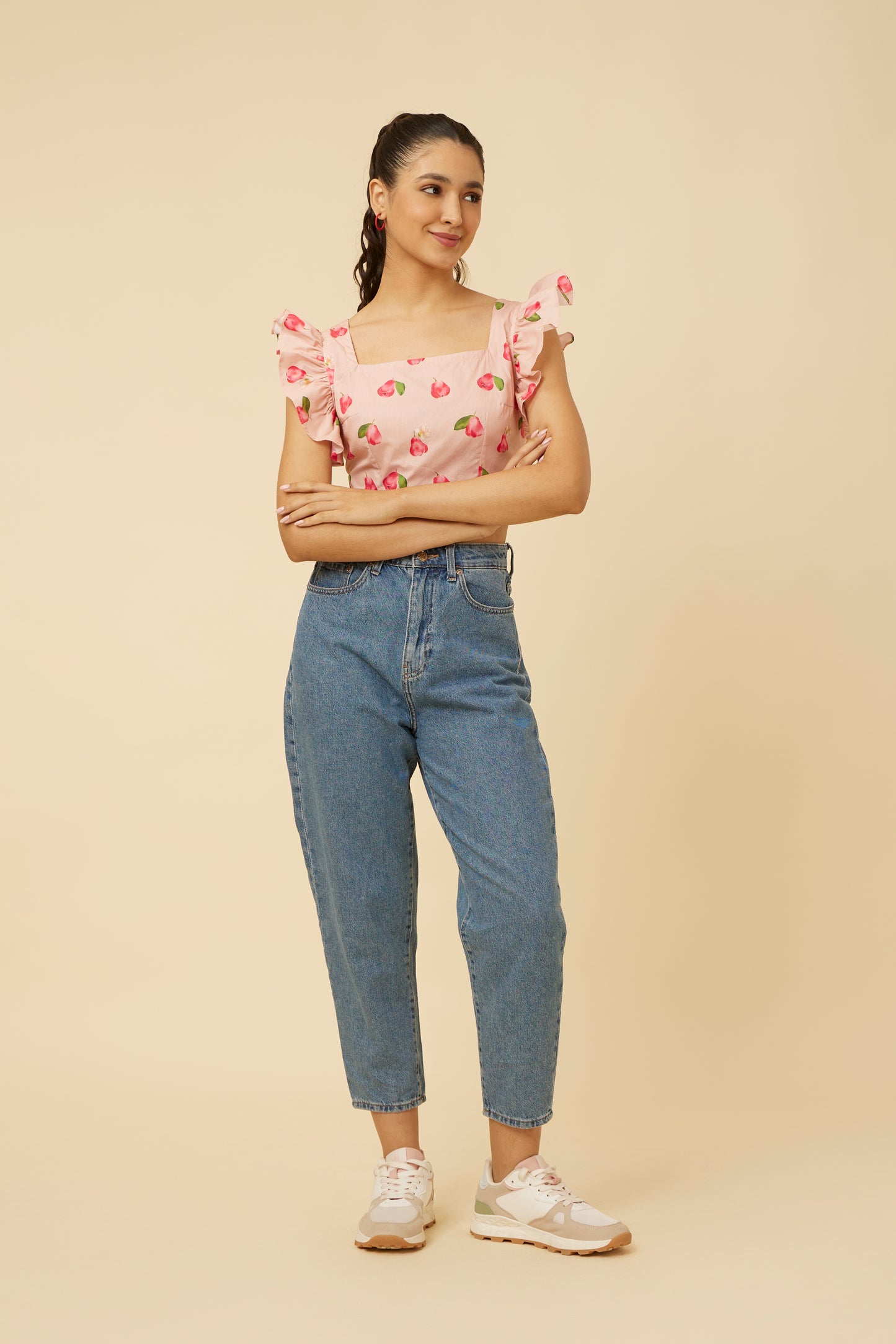 Confident woman standing in a Rose Apple Frill Crop Top featuring feminine shoulder frills and a sleeveless design, complemented by casual denim pants