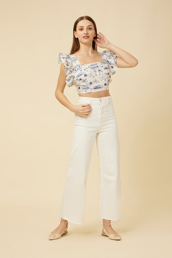 Homeland Frill Crop Top featuring sleeveless design and feminine shoulder frills, elegantly paired with relaxed-fit white pants and open-toe sandals