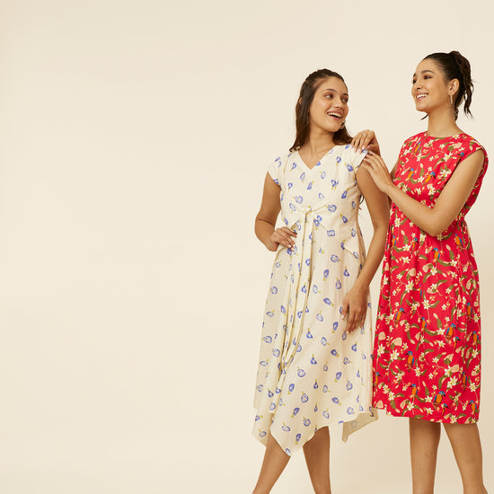 Two radiant young women presenting Hypsway's bespoke summer dresses; one wearing a light blue midi dress with delicate lavender floral patterns and a waist tie, and the other in a red knee-length dress with bold yellow floral prints, both exuding casual elegance and contemporary style, ideal for the fashion-conscious young Indian woman.